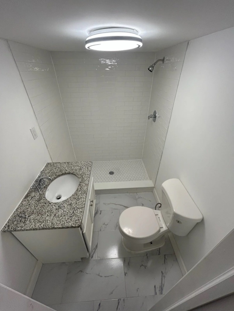 Renovated bathroom with subway tile shower, granite vanity, and marble tile floor